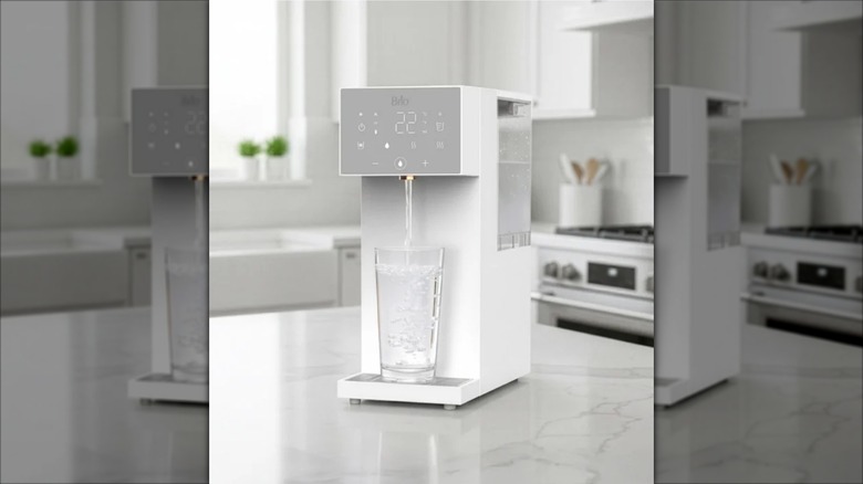 Su pınarı mutfak tezgahının üzerinde duruyor, şeffaf bir bardağa su döküyor.