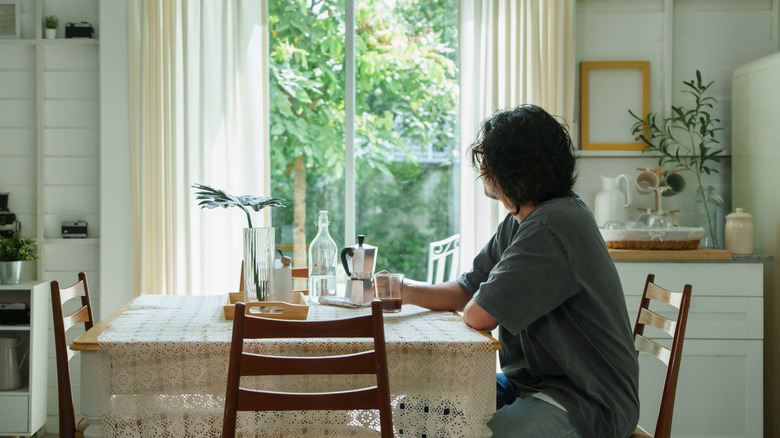 Mutfak masasında oturan biri pencereden dışarı bakıyor.