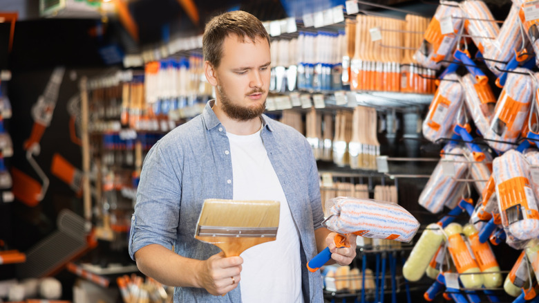Ev dekorasyon mağazasında boya fırçası ve ruloya bakan adam