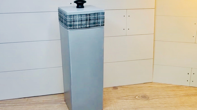 Plastik torba deposuna dönüştürülen şarap kutusu, duvara monte edilmeden önce tezgahın üzerinde duruyor.