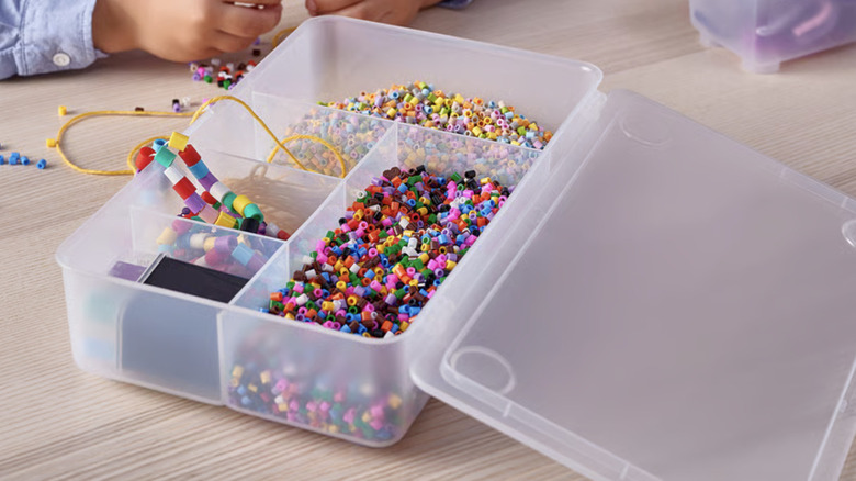 Ahşap el işi masasının üzerinde renkli boncuklarla dolu şeffaf bir IKEA GLIS kabı.