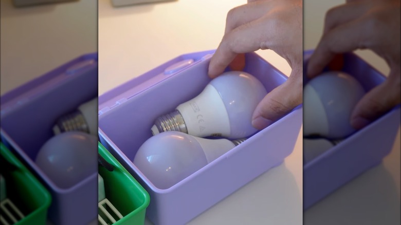 Bir kişi küçük mor bir IKEA GLIS kutusuna bir ampul yerleştiriyor.