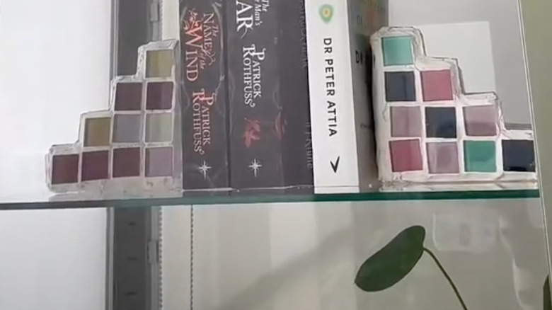 Üç kitabı destekleyen cam kitaplık üzerinde karton tabanlı, fayanslı kitap ayraçları.