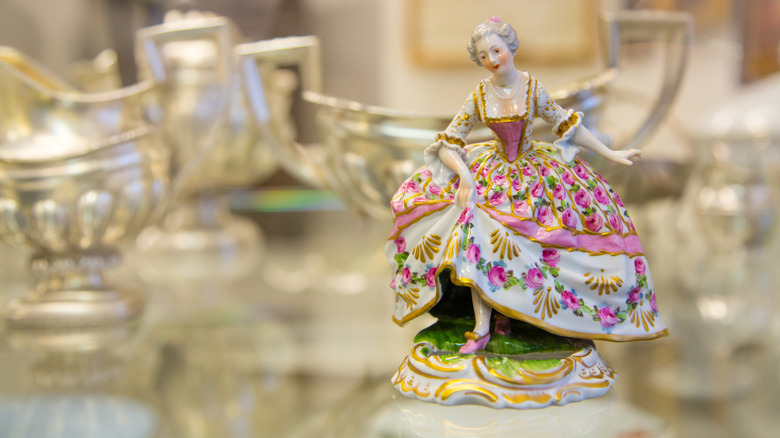 Gümüş eşyalar arasında porselen bir heykelcik.