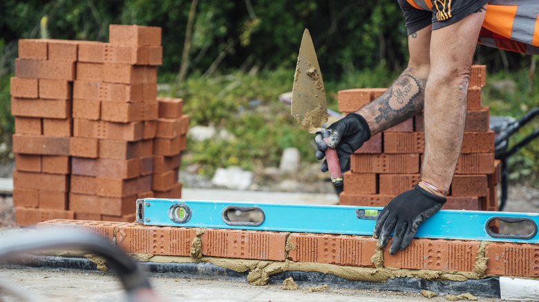 Bahçeye düzgün bir tuğla geçit kurmak için mala ve terazi kullanan adam.