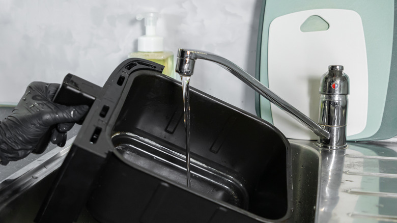 Siyah eldiven giyen kişi, fritöz sepetini lavabodan suyla dolduruyor