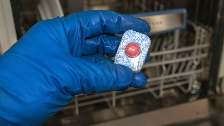 Eldivenli el bulaşık makinesi tabletini tutuyor