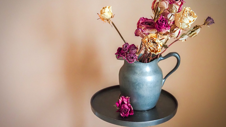 Kurutulmuş çiçekler tutan küçük bir masanın üzerinde duran kalaylı sürahi