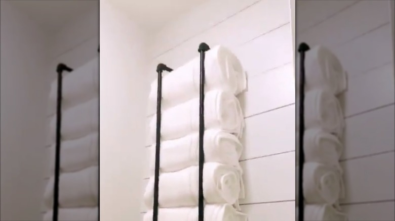 Dikey siyah borulardan yapılmış, içine beyaz havlular sarılmış bir DIY havlu askısı