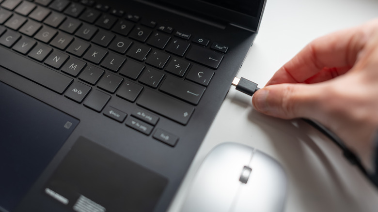 Şarj kablosunu dizüstü bilgisayara bağlayan bir el.