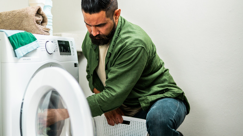 Adam çamaşır makinesinden çamaşır çıkarıyor.