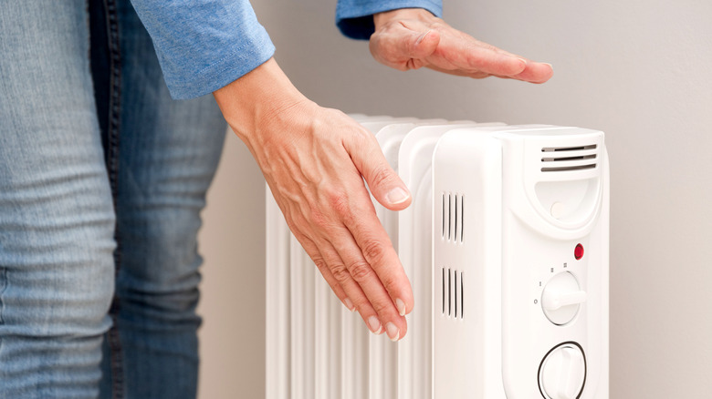 Radyatörlü ısıtıcının yanında ellerini ısıtan bir kişi.