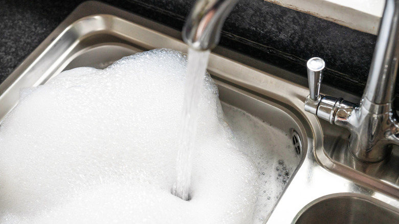 Sabun köpüğüyle dolu paslanmaz çelik lavaboya akan musluk