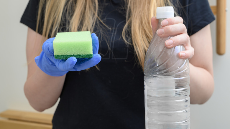 Sarışın kadın elinde sirke şişesi ve sünger tutuyor