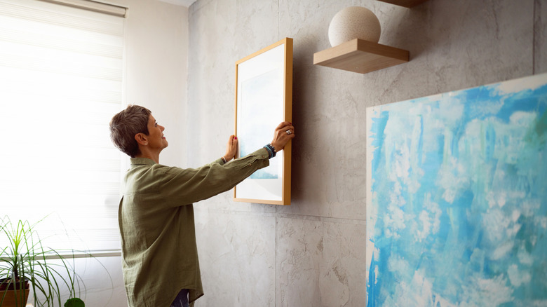 Çerçeveli bir sanat eserini diğer sanat sergilerinin yanındaki duvara koyan kadın