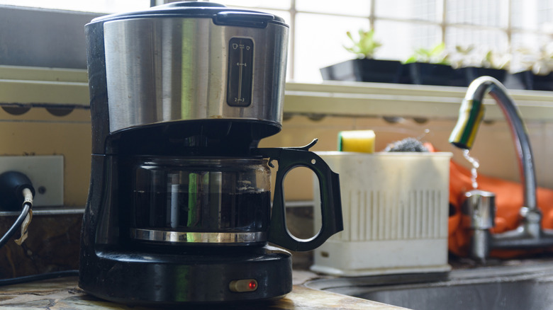 Lavabo ve musluğun yanında duran bir kahve makinesi.