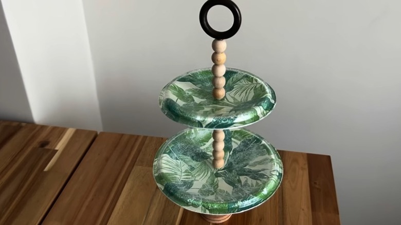 Tencere kapaklarından yapılmış iki katmanlı bir pasta standı ahşap bir masanın üzerinde duruyor.