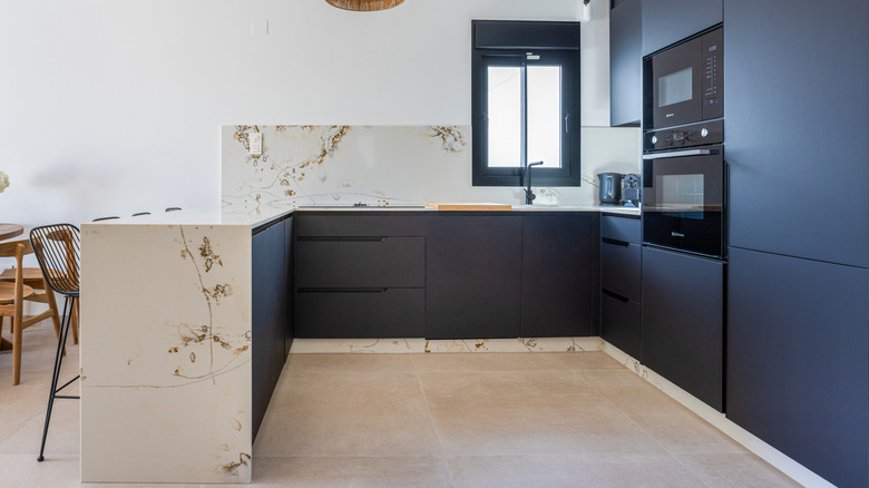 koyu renkli dolaplara ve geniş formatlı karo zeminlere sahip açık konseptli bir mutfak