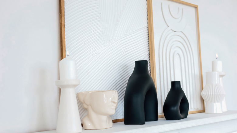 Çerçeveli sanat eserleri, mum ve aksesuarlar sade beyaz şömine rafının üzerinde duruyor