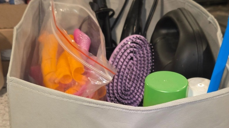 Kumaş saklama kutusunda saç aletleri, rulolar ve spreyler