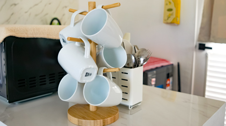 Mutfak dolabının üzerinde, arkasında çatal-bıçak düzenleyici bulunan kupa tutucu ağaç.