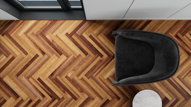 Koyu desenli balıksırtı ahşap zeminin kuş bakışı görünümü, koltuk ve yan sehpa