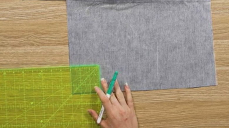 Marker tutan bir el, kumaşın üzerine bir ölçüm aleti yerleştirir.