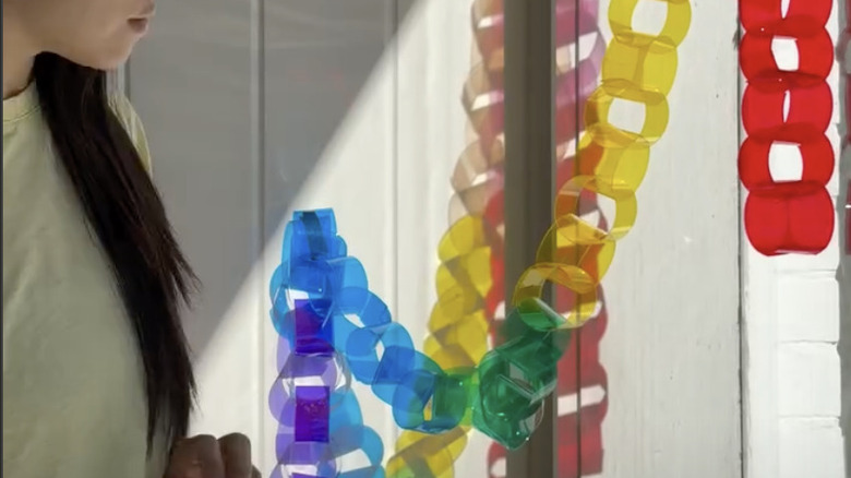 Pencerenin yanında duran ve camın önünde ışığı filtreleyen kağıttan yapılmış bir güneş yakalayıcı asılı olan kadın