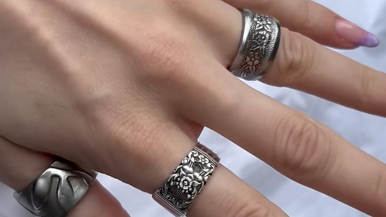 Tasarruflu gümüş kaşıklardan yapılmış yüzüklerle süslenmiş bir el.