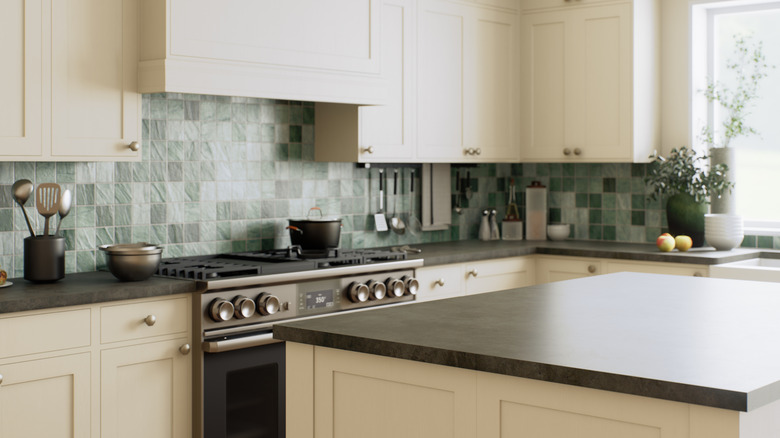 Yeşil backsplash ve krem ​​​​dolapları olan bir mutfak