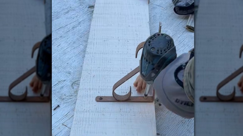 Beyaz bir rafa braket takmak için elektrikli tornavida kullanan biri.