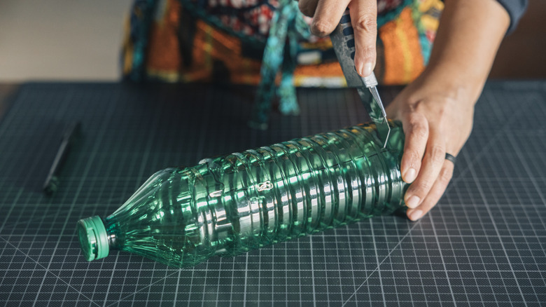 Maket bıçağıyla plastik şişeyi kesen kişi.