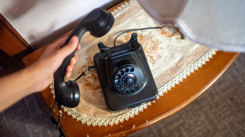 Küçük bir masanın üzerinde çevirmeli telefon tutan bir kişi