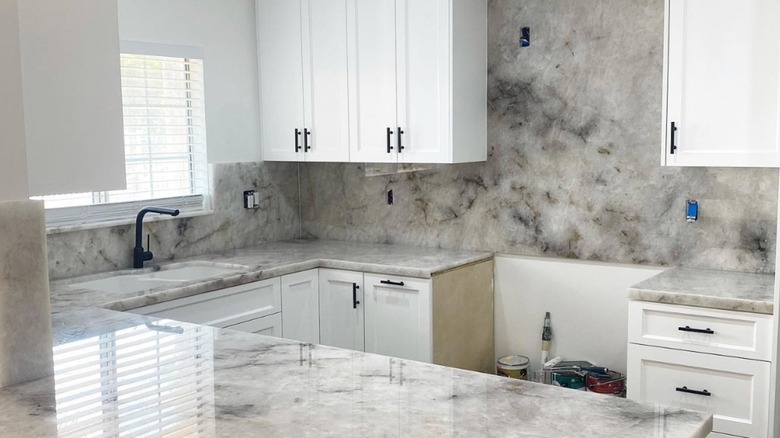 Beyaz dolaplı, yakın zamanda yenilenmiş bir mutfakta beyaz kuvarsit levha backsplash
