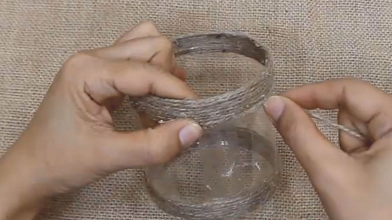 Tuvalet kağıdı tutucusu yapmak için plastik bir tüpün etrafına ip saran kişi