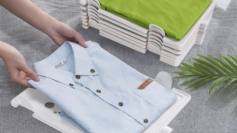 Bir kişi katlanmış bir gömleği, gömlekli diğer düzenleyicilerden oluşan bir yığının yanındaki istiflenebilir plastik bir düzenleyicinin üzerine koyar.