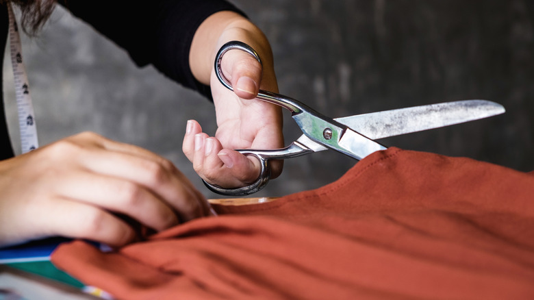 Bir çift açık tenli el turuncu kumaşı makasla kesti.