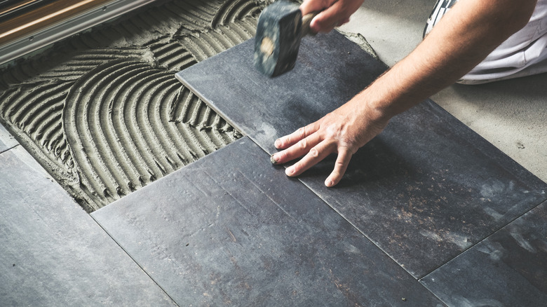 Bir odadaki büyük koyu renkli fayansları çekiçle vuran bir kişi