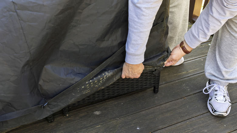 veranda mobilyalarını örtmeye çalışan kişi