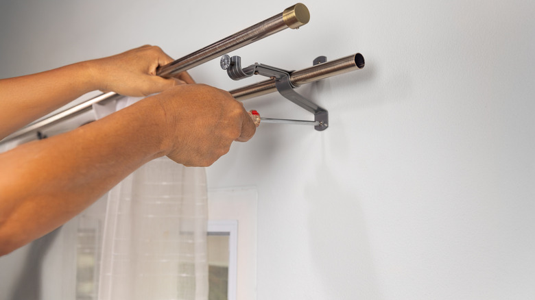 Eller perde çubuğunu asar.