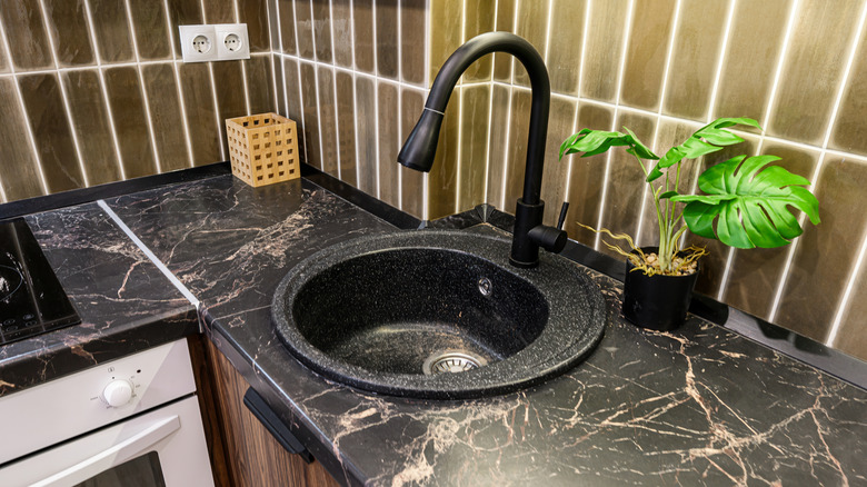 Kahverengi dolap ve backsplash ile siyah mermer tezgah üzerinde siyah mutfak lavabosu
