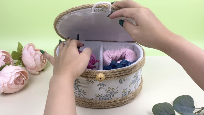 Bir kişi saç tokalarını ve diğer saç aksesuarlarını kumaş kaplı bir DIY kutusuna koydu.