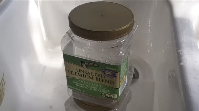 Mutfak lavabosunda büyük altın kapaklı, tuzsuz fındıklarla dolu boş bir plastik kap.