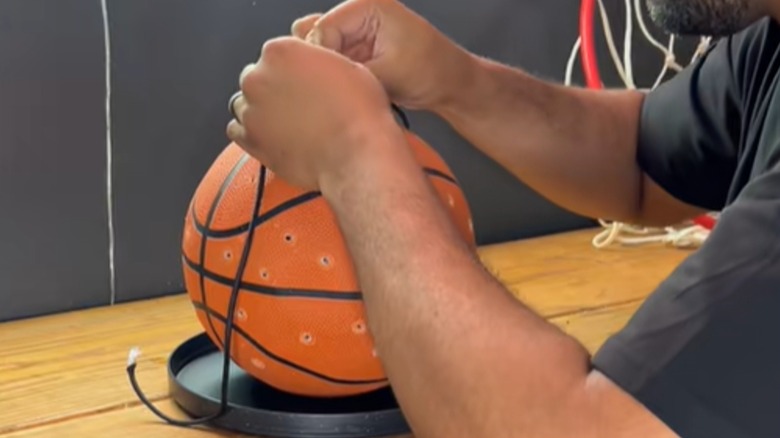Bir adam, çevresine delikler açılmış basketbol kuş besleyicisine askı ipleri bağlıyor