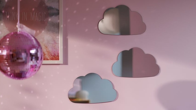 Bulut şeklindeki aynalar pembe bir duvarda, çerçeveli bir fotoğrafın ve pembe bir disko topunun yanında sergileniyor.
