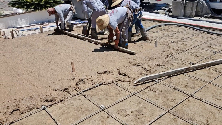 Bir grup işçi bej beton bir araba yolu döşüyor
