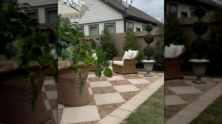Dama tahtası verandası, rattan dış mekan mobilyaları ve saksı budama çiçekleriyle konutun arka bahçesi.