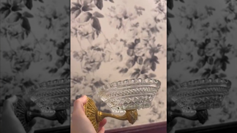 Bir el, cam mumluk ve pirinç kancadan yapılmış bir DIY sabunluk tutuyor.