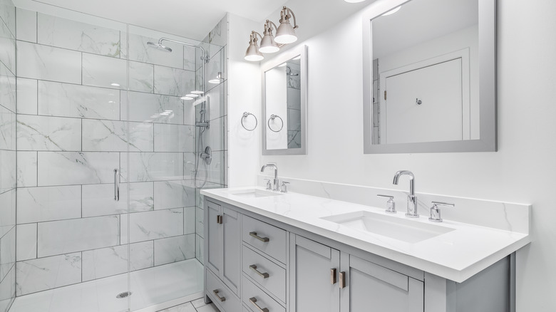 Gri bir makyaj masası ile birden fazla krom armatür ve bağlantı parçasına sahip gri kiremitli bir banyo