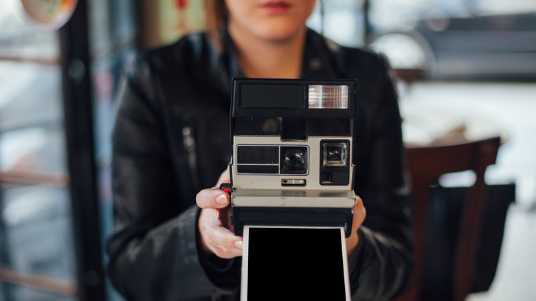 Eski bir Polaroid kamerayla fotoğraf çeken bir kadın.
